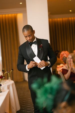 Person in tuxedo reading a speech at an elegant reception.