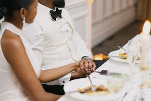 Couple holds hands intimately at an elegant wedding reception dinner table.