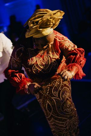 Dancer in ornate gold headpiece and red patterned dress performs under blue lighting.