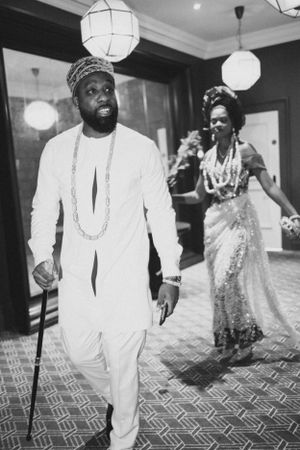 Couple in traditional white attire walking under pendant lights at formal event.