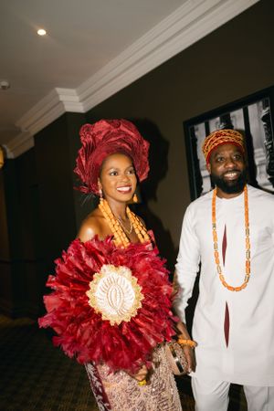 Couple in traditional African attire with red floral decor at celebration.