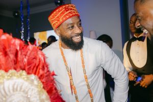 Man wearing traditional Nigerian wedding attire with orange beaded necklaces smiles during celebration.