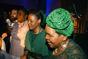 A group of guests dancing and celebrating at an elegant evening event with blue lighting and decorative headwear.