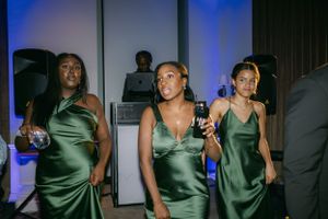 Bridesmaids in elegant emerald green satin dresses pose during wedding reception.