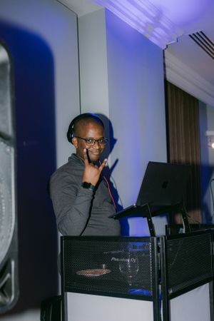 Wedding DJ wearing headphones and glasses performs at reception behind professional equipment setup.