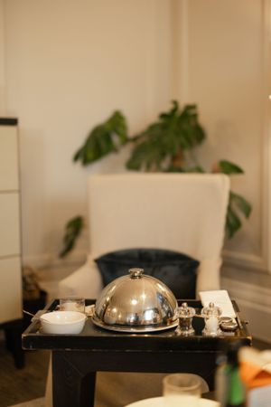 Room service setup with silver cloche dome on black tray with monstera plant in background.