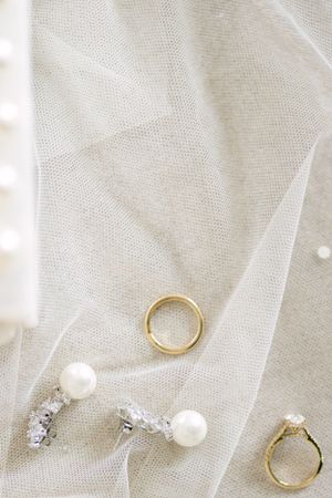 Gold wedding ring and pearl earrings arranged on delicate white tulle fabric.