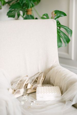White bridal accessories and shoes displayed on a chair with monstera leaves in background.
