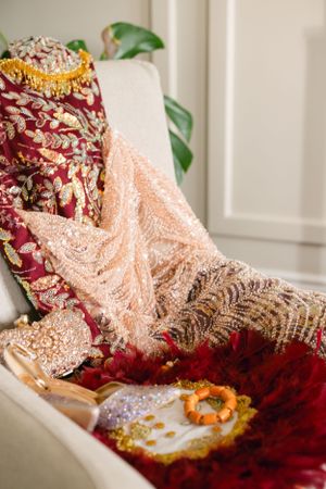 Luxurious red and gold embroidered wedding dress with delicate lace details laid on a white sofa.