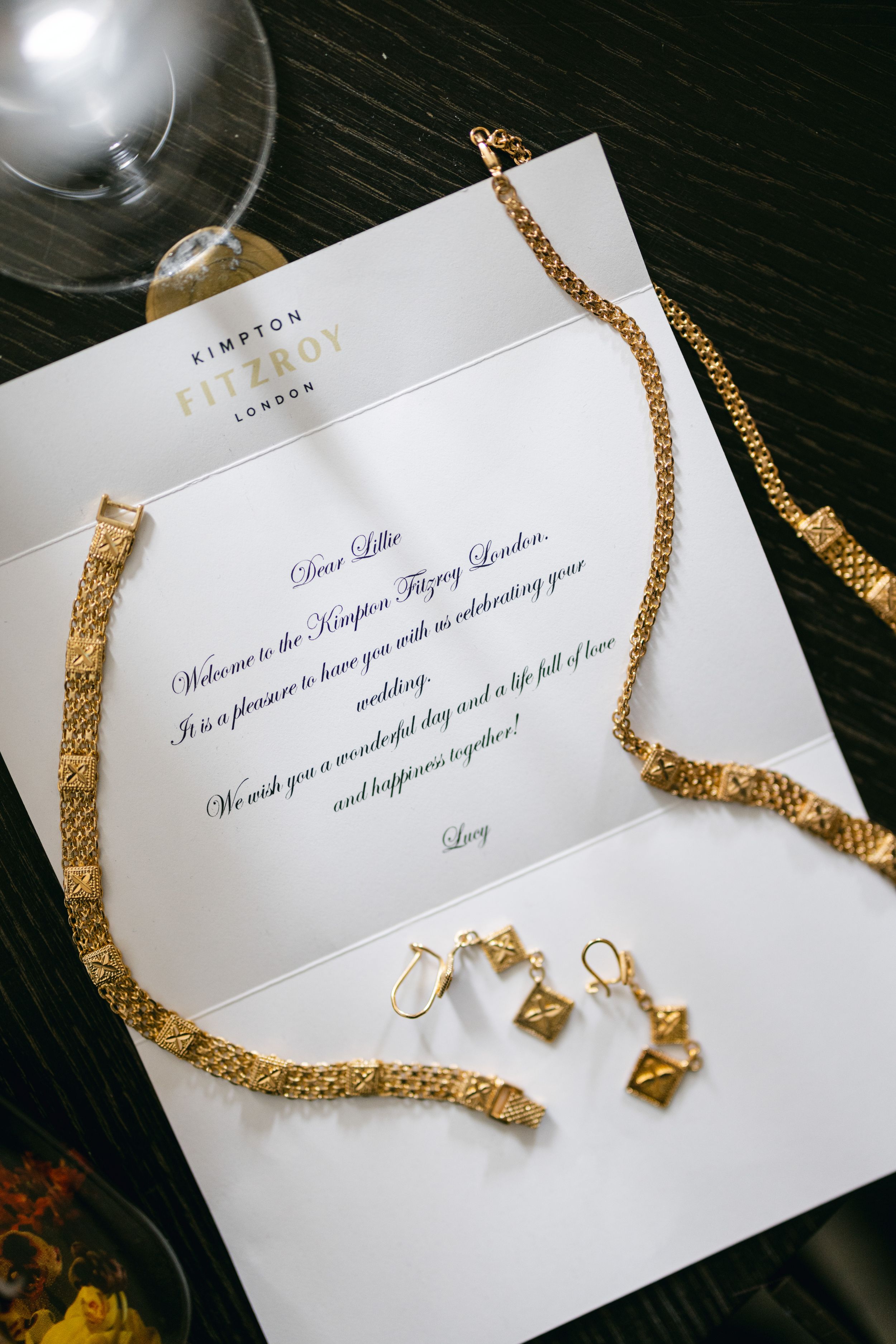 Wedding invitation with gold jewelry and necklace on dark surface.