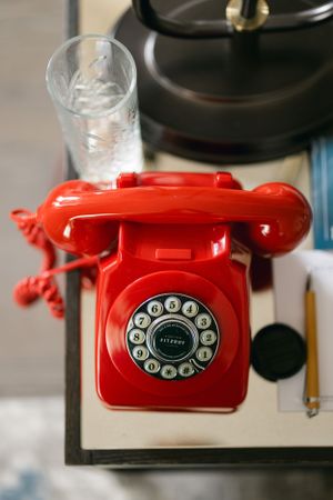 Vintage-style red rotary telephone with circular dial on a dark surface.