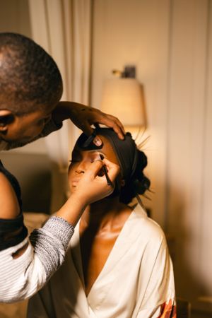 Warm-toned interior scene showing makeup application in soft lighting.