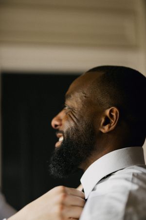 Side profile of a person with a beard smiling and adjusting collar of white dress shirt.