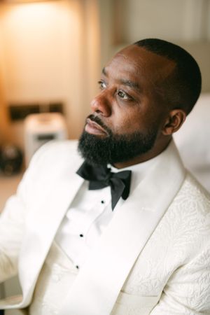 Stylish wedding attire featuring a white tuxedo jacket with black bow tie and detailed lapels.