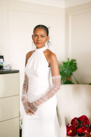 Elegant bride in white halter neck gown with sheer long sleeves and natural makeup.