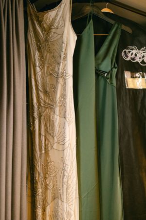 Elegant wedding dress and bridesmaid gown in sage green hanging on display.