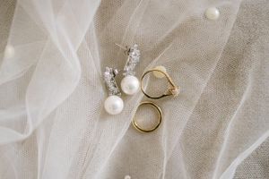 Wedding rings and pearl earrings arranged on delicate white tulle fabric.