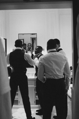 Black and white photo of groomsmen getting ready in formal attire before wedding ceremony.
