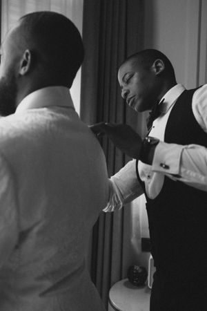 Black and white image of wedding preparations showing formal wear adjustments.