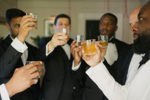 Groomsmen in tuxedos raise glasses for a celebratory toast at a wedding reception.