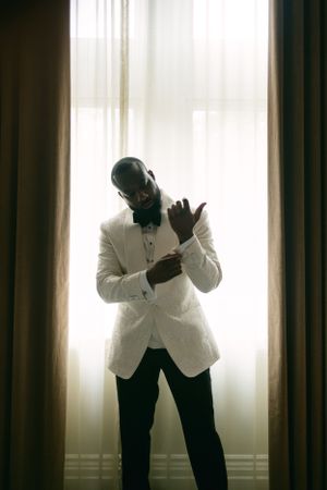 Silhouette of person in white jacket adjusting cuffs against bright window.
