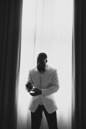 Silhouetted figure in white jacket stands against bright window in dramatic black and white photo.