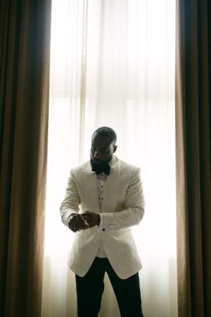 A silhouette of a person in a white tuxedo jacket standing by a bright window.