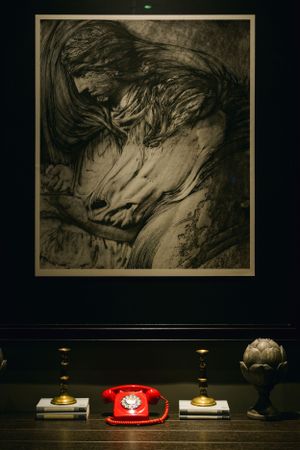 Dramatic artwork with red vintage telephone displayed beneath on wooden table.