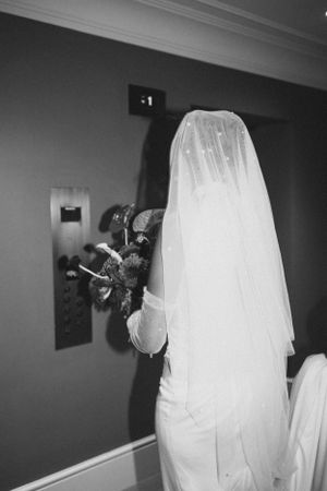 Black and white photo of bride in flowing veil from behind.