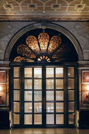 Ornate illuminated archway with decorative fan-shaped transom window and glass double doors.
