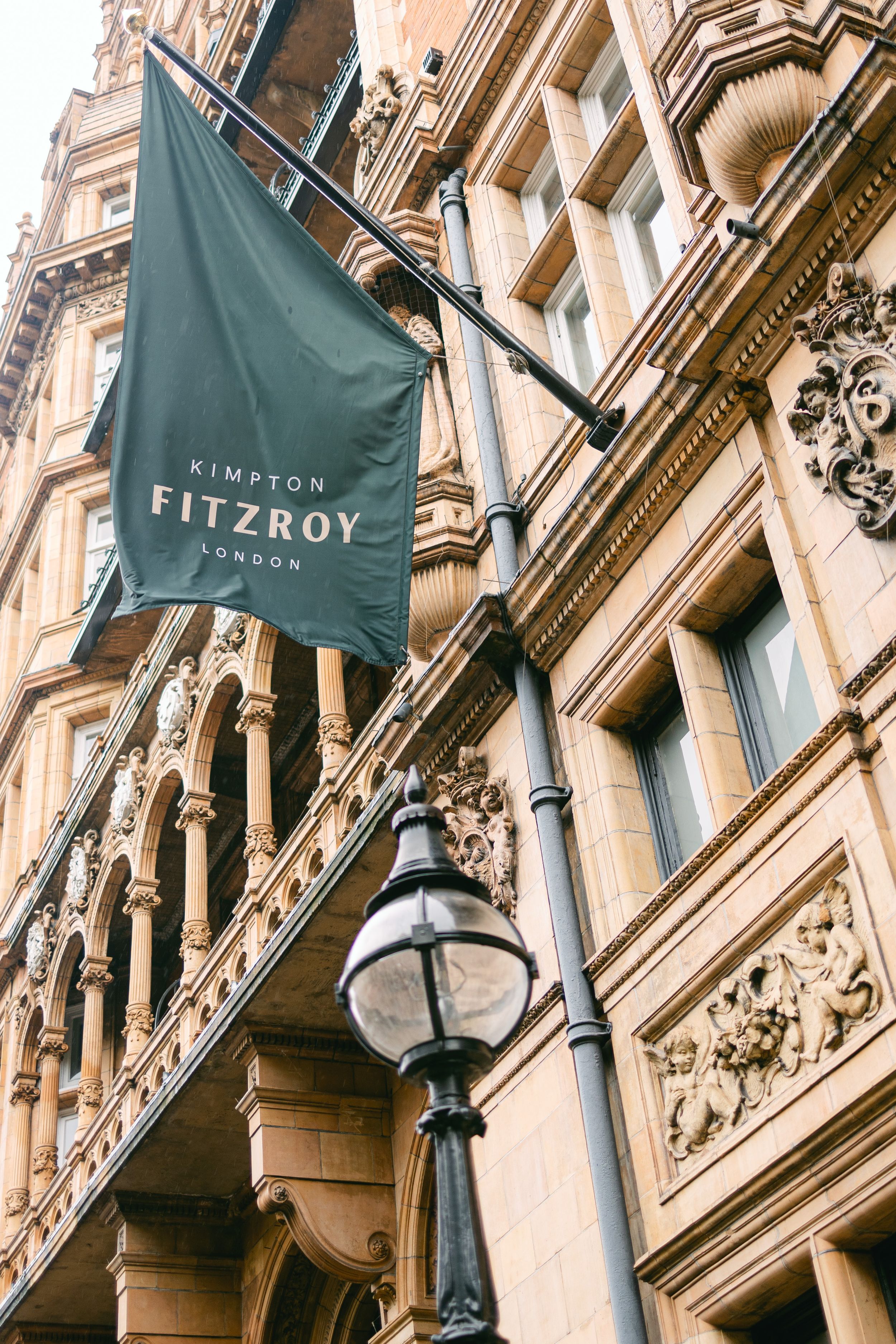Elegant Kimpton Fitzroy hotel flag and vintage lamp post against ornate Victorian architecture in London.