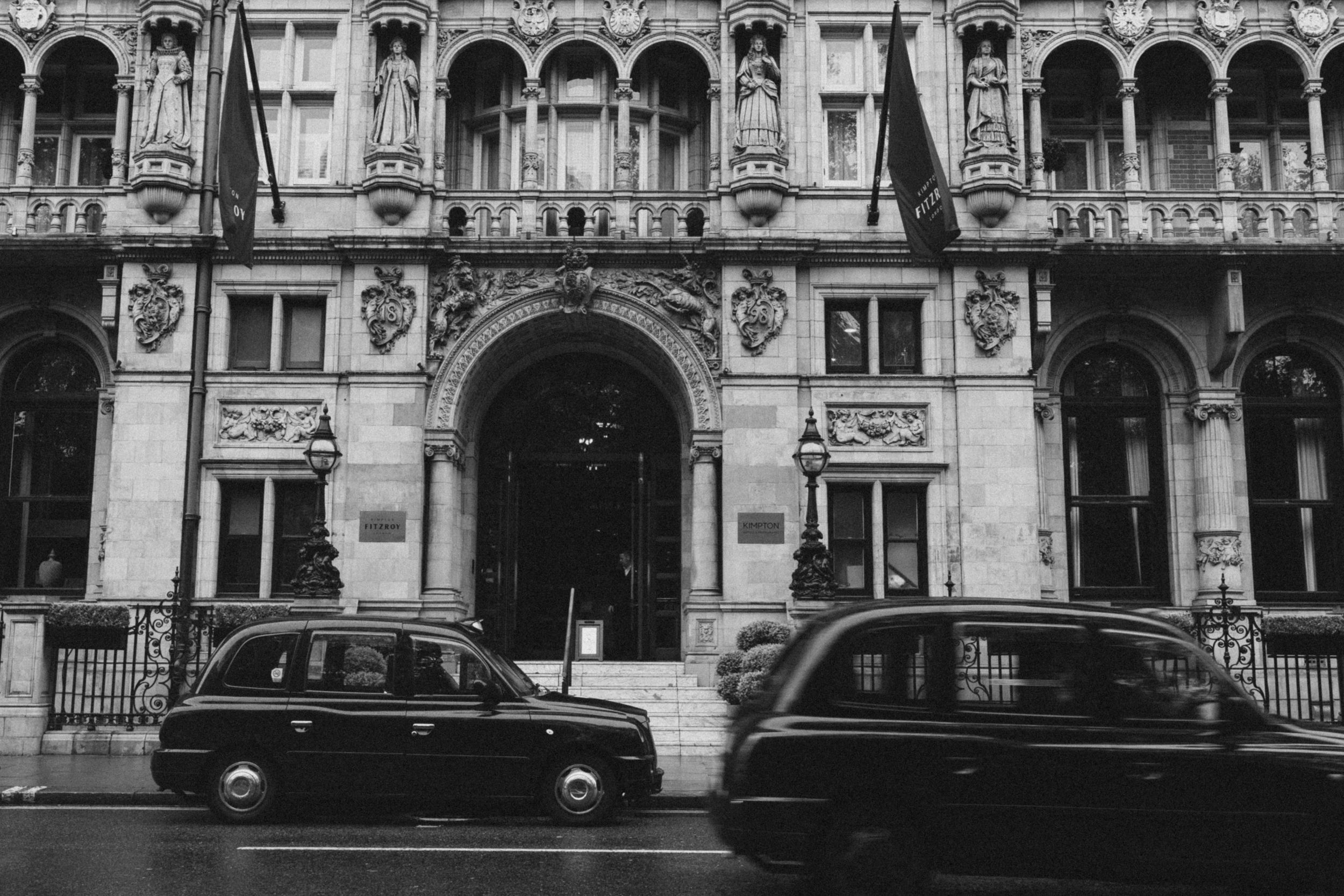 Classic black London taxis parked in front of an ornate Victorian building with arched windows.