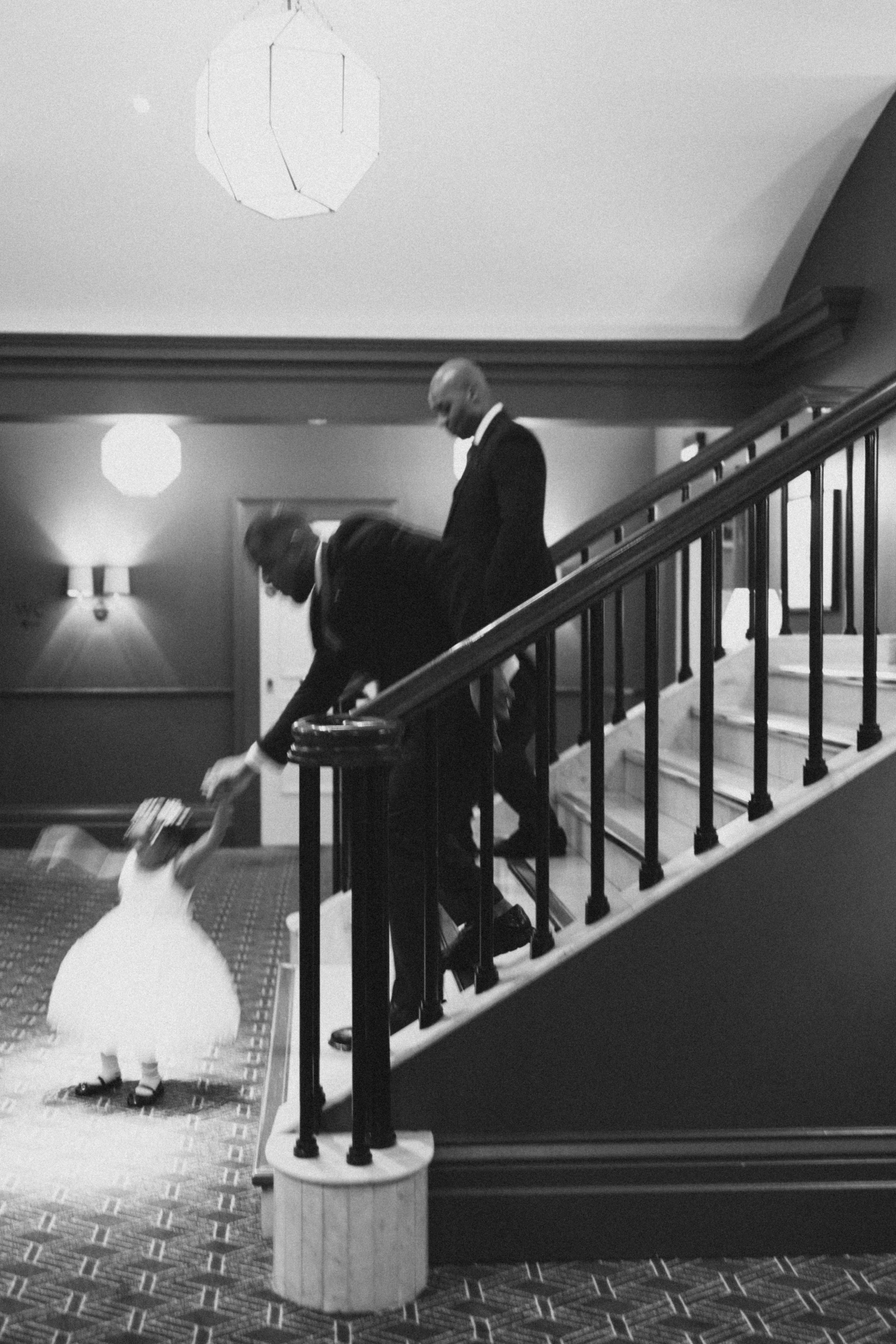 Black and white photo of wedding party descending elegant staircase with patterned carpet.