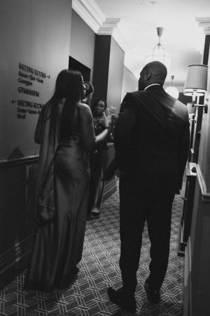 Elegant formal gathering in a hotel hallway with guests in evening attire.