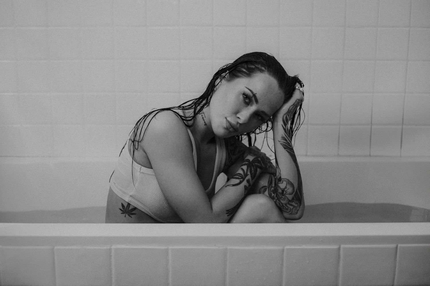 Black and white portrait showing contemplative pose against bathroom tiles.