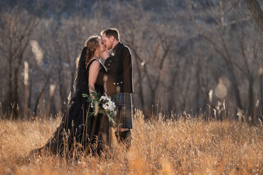 Wedding couple poses in a rustic autumn field with bare trees and golden grass.