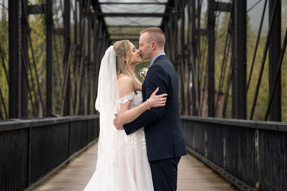A romantic wedding couple shares tender moments on a rustic iron bridge surrounded by trees.
