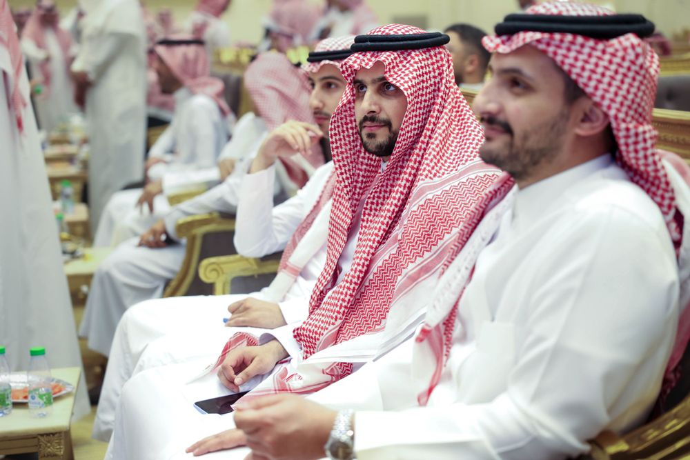 يستمتع ضيوف الحفل بالجلوس وتبادل الحديث. يظهرون مبتسمين ويرتدون الأزياء السعودية التقليدية الثوب والشماغ بأناقة.