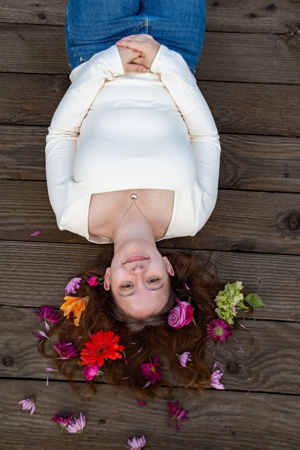 Person lying on wooden deck surrounded by colorful flowers including red, purple and pink blooms.