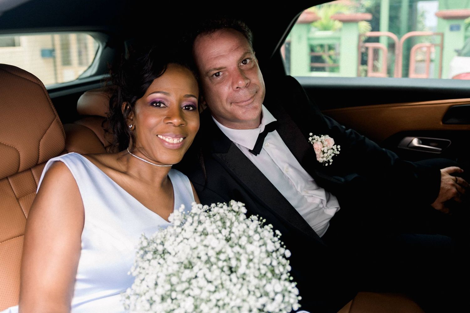 Mariés à l'arrière d'une voiture souriant avec un bouquet de fleurs blanches