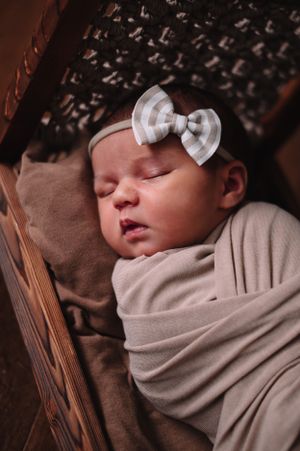 A sleeping newborn baby wearing a bow headband swaddled in neutral fabric.