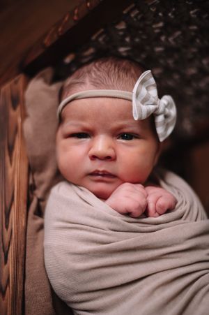 A swaddled newborn baby with a bow headband gazes at the camera.