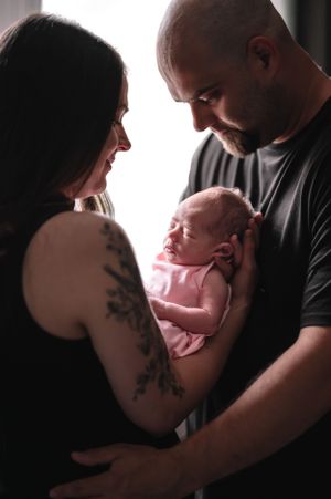 Parents in black clothing share intimate moment while holding their newborn baby in pink.