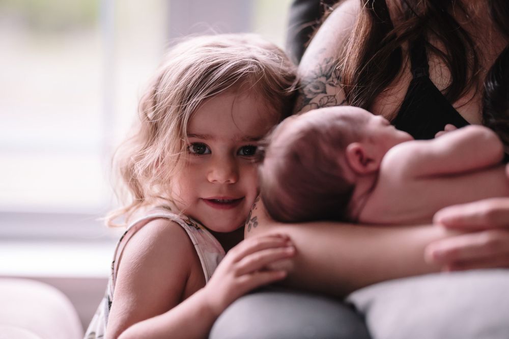 Young child leans in close to look at sleeping newborn during family portrait session.