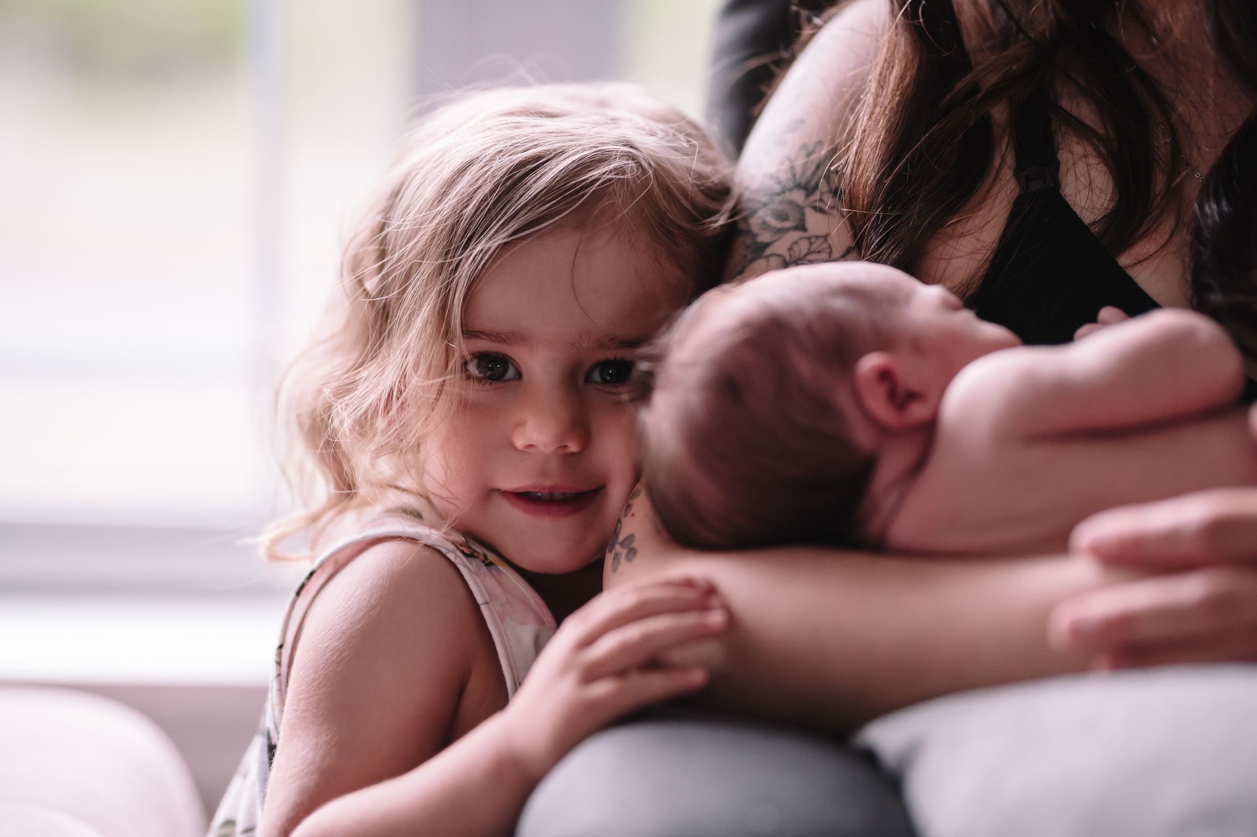 Young child leans in close to look at sleeping newborn during family portrait session.
