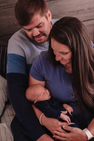 Intimate family moment with newborn baby sleeping between parents on wooden background.