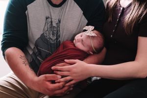 A newborn baby rests peacefully in their parents' arms wearing a bow headband.