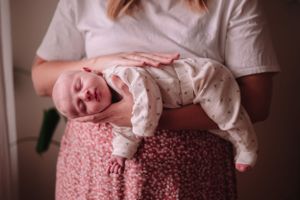 Baby in white outfit crying while being held against floral pink dress.