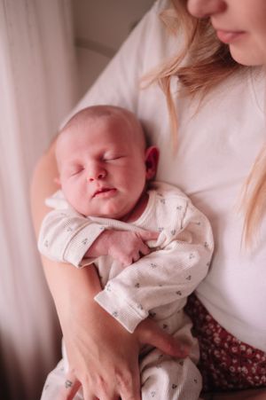 Peaceful newborn in white dotted outfit sleeping against white clothing.