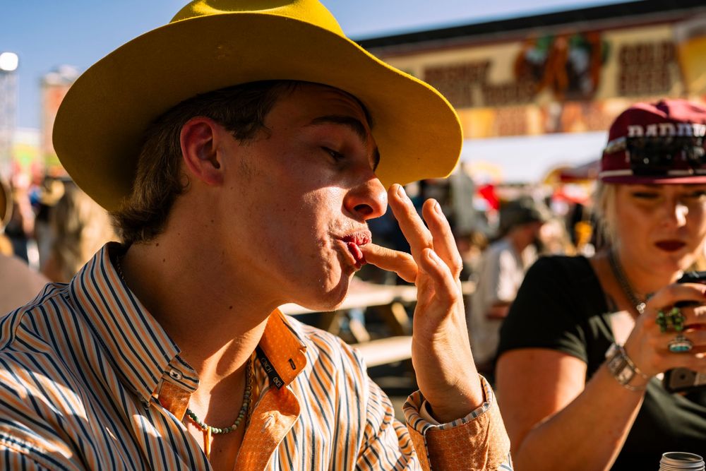 Young man in yellow cowboy hat smoking at outdoor festival event.